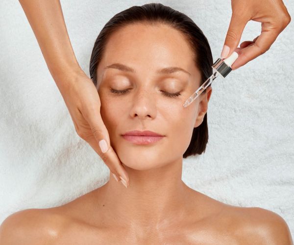 Frau mit geschlossenen Augen, Hand stützt die Wange, Pipette träufelt Serum aufs Gesicht